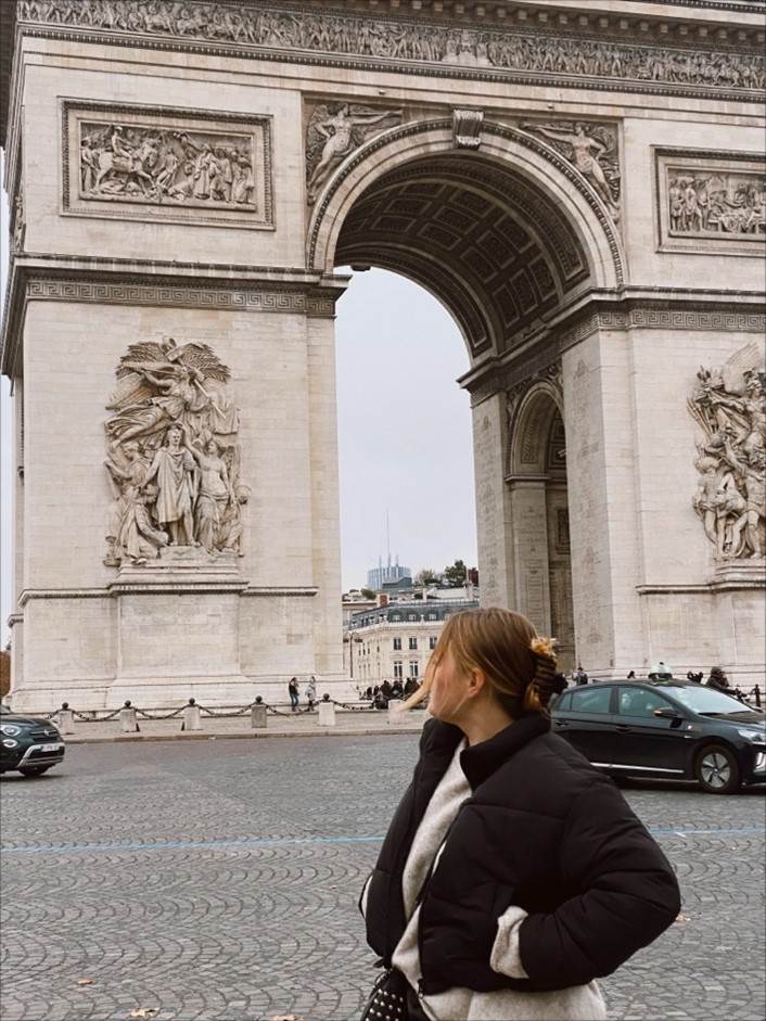 a young woman stands in front of the arc du triomphe