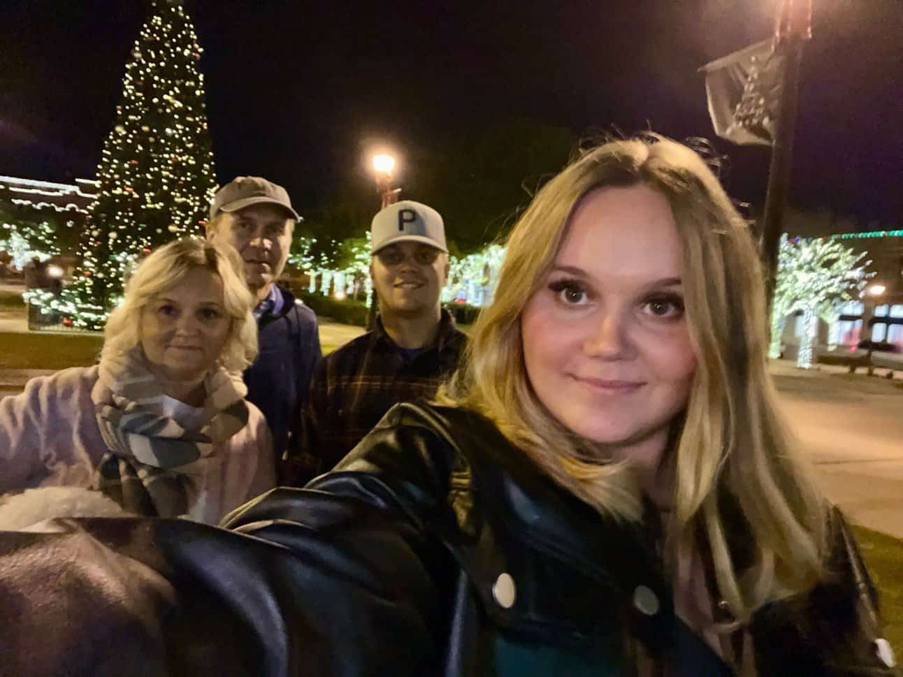 a selfie of a family, taken by a young girl in front of a christmas tree at night