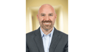 an image of a smiling bald man with a beard in a grey blazer and light blue shirt