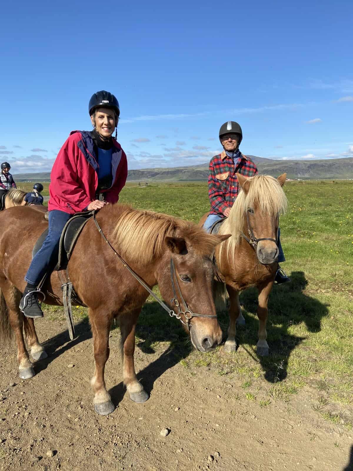a woman and a man sit atop a pair of horses, smiling
